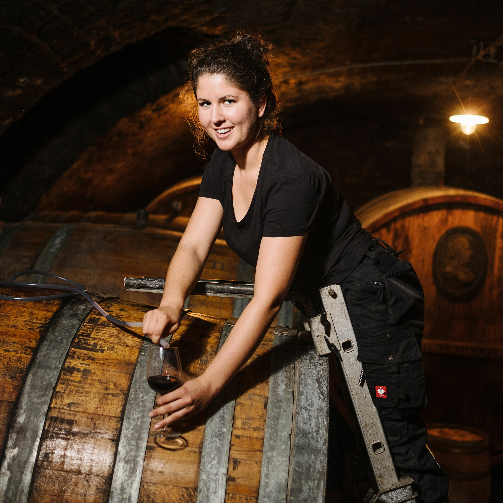 Étudiante en viticulture lors du prélèvement d'un échantillon de vin rouge dans la cave à barriques de son entreprise de coopération à Neustadt