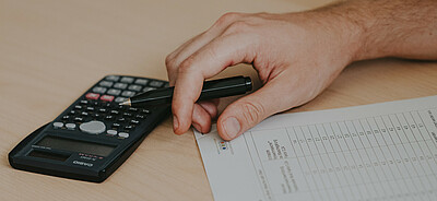 Calculatrice posée sur la table à côté d'une main tenant un stylo