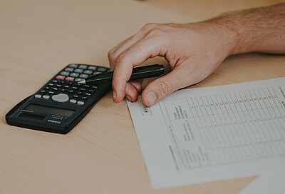 Calculator, papers and hand with pen on a table