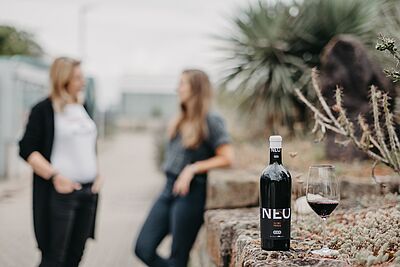 NEO Wein im Vordergrund, im Hintergrund ein Gespräch zweier Personen